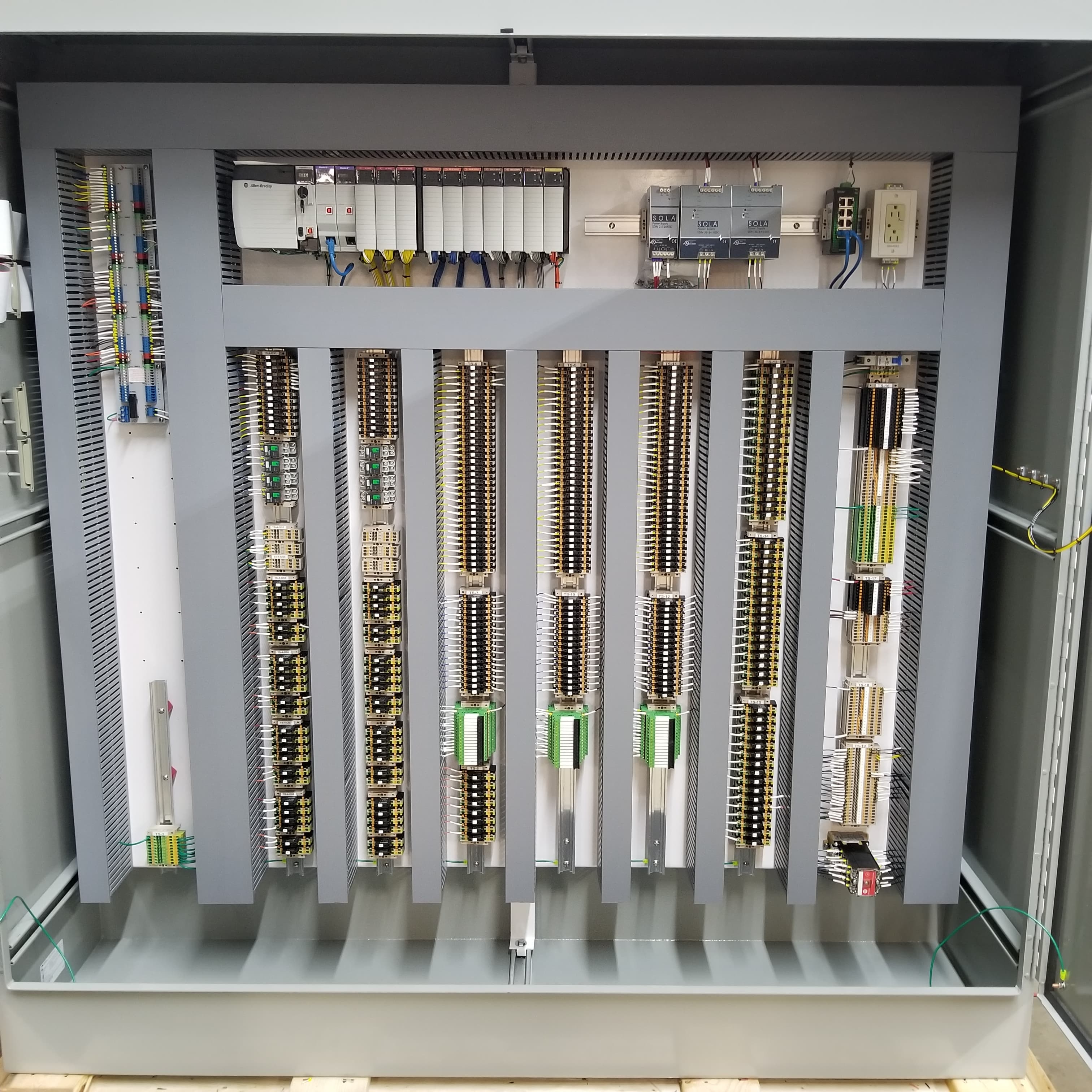 Organized industrial electrical control panel with PLCs, power supplies, and vertical rows of terminal blocks.